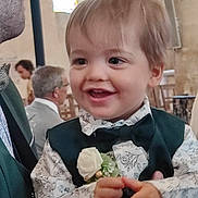 Aïden participe au concours pour gagner de l'argent avec cette photo : toddler, child, smiling, formal_clothing, bow_tie, vest, flower, indoor, event, people, adult, glasses, stained_glass, background, portrait, happy, hands, face, short_hair, ceremony