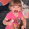 toddler, child, pacifier, pink_shirt, indoor, toy, blanket, couch, curious, person, young_child, short_hair, cartoon_print, furniture, home, casual_clothing, portrait, smiling, baby, cute