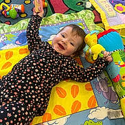 Isabella is registered to the contest to win money with this photo: baby, bright_colors, carpet, child, colorful, crawling, cute, floor, happy, indoor, infant, lying_down, pacifier, patterned_clothing, person, play_mat, playing, smiling, soft_toy, toy