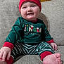baby, child, smiling, pajamas, hat, striped_clothing, christmas, holiday, couch, furniture, indoors, cute, happy, infant, seated, person, wood_paneling, cozy, red, green