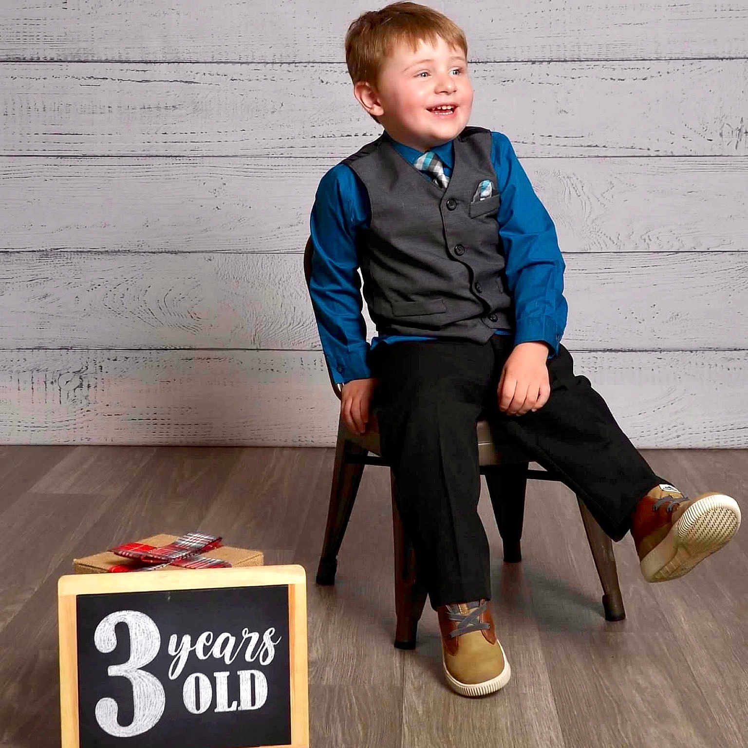 Paulie is registered to the contest to win money with this photo: blackboard, boy, child, clothing, coat, face, footwear, head, jacket, jeans, male, pants, person, photography, portrait, shoe, sitting, sleeve, text, wood