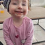 Kessy a rejoint le concours — aidez-le/la à gagner de superbes lots ! toddler, child, smiling, hat, beret, pink_shirt, face, messy_face, indoor, living_room, table, cartoon_tv, floor, tile_floor, cute, happy, person, clothing, young_child, home