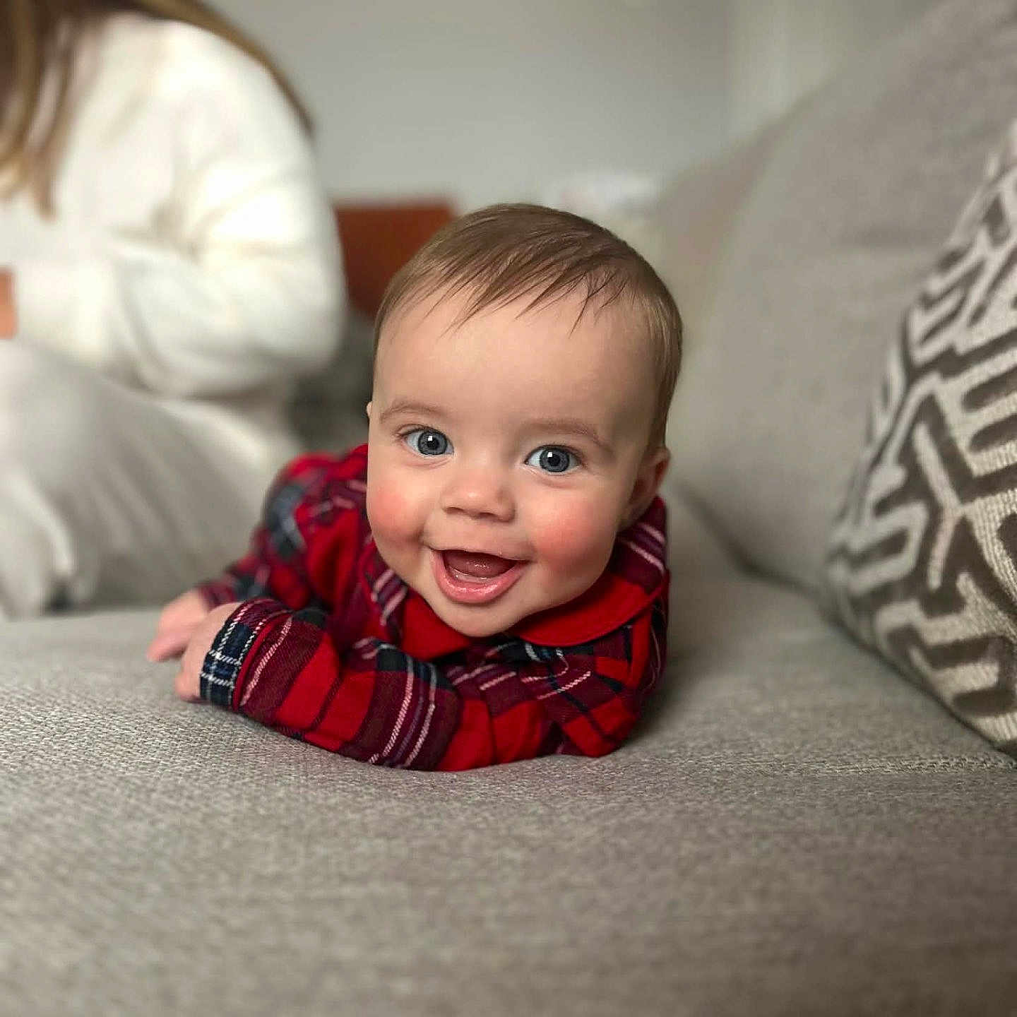 James-Junior is registered to the contest to win money with this photo: baby, blue_eyes, blurred_background, casual_clothing, child, couch, cozy, face, gray_couch, happy, home, indoor, infant, patterned_pillow, person, pillow, plaid_shirt, portrait, smiling, soft_light
