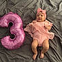baby, pink, balloon, number_three, headband, blanket, infant, cute, celebration, lying_down, clothing, soft_fabric, smile, child, portrait, indoors, skin, feet, hands, adorable