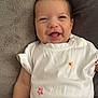 baby, smiling, onesie, white_clothing, embroidery, flower, infant, happy, lying_down, blanket, pillow, cozy, cute, child, skin, head, face, arm, leg, indoor