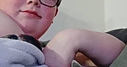 Ander Dingus is registered to the contest to win money with this photo: blanket, casual, cat, child, comfort, cozy, cute, furniture, glasses, gray_cat, home, indoor, paw, portrait, relaxed, sitting, snuggling, soft_texture, stretching, warm