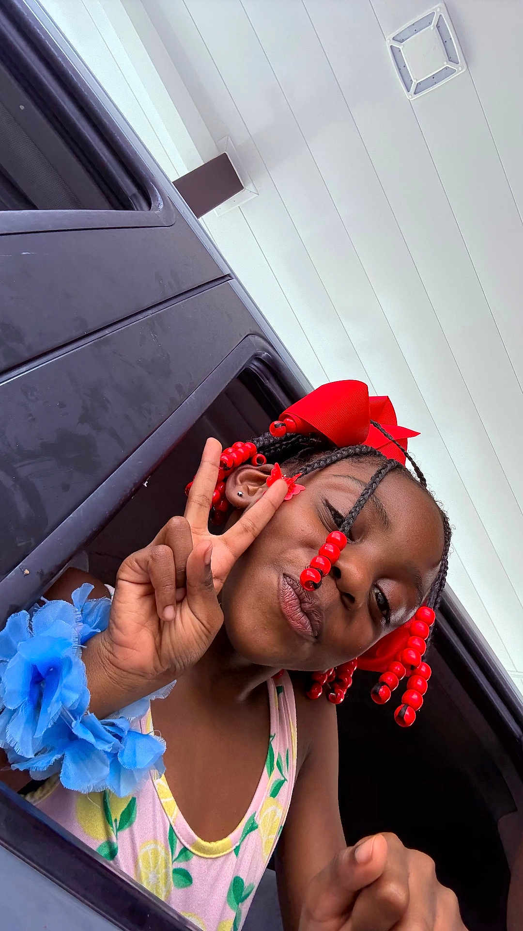 Gracelyn joined the competition — help win amazing prizes! child, girl, peace_sign, braids, red_beads, red_bow, blue_flower_bracelet, car_window, smile, summer, lemon_pattern, tank_top, portrait, happy, playful, outdoor, skin, hand_gesture, accessory, youth