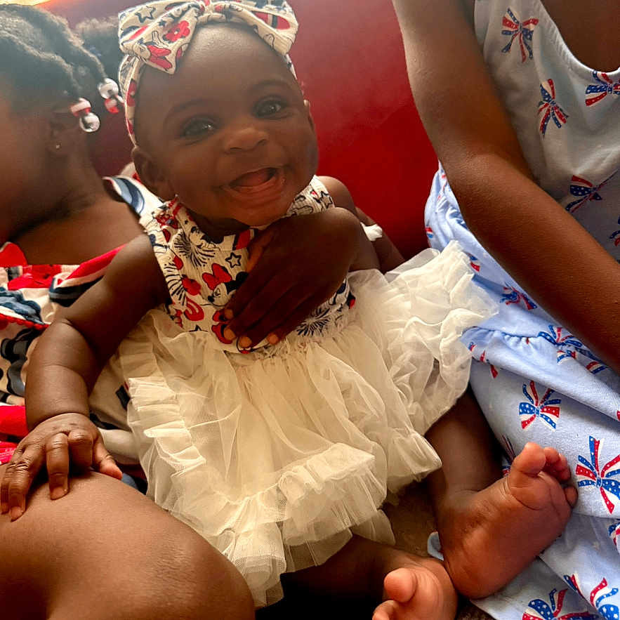 Kayceelyn joined the competition — help win amazing prizes! baby, child, closeup, couch, dress, family, foot, hand, happy, headband, indoor, patterned_clothing, people, portrait, red_background, sitting, skin, smiling, three_children, toddler