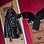 cat, black_and_white, collar, dresser, door, jacket, camouflage, coat_hook, red_wall, wooden_furniture, indoor, pet, feline, curious, sniffing, clothing, handle, room, domestic, domestic_cat