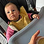 baby, child, high_chair, bib, pink_clothing, feeding, food_container, hand, blue_eyes, indoor, table, plastic_tray, curly_hair, messy_bib, person, face, expression, looking_up, skin, infant