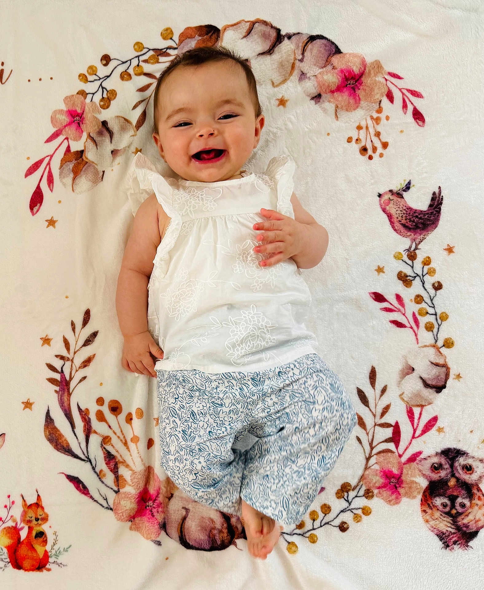 Kélia participe au concours pour gagner de l'argent avec cette photo : baby, smile, child, blanket, floral_pattern, woodland_animals, cute, lying_down, happy, white_clothing, patterned_pants, infant, face, portrait, indoors, soft_texture, decorative, cozy, small_child, playful