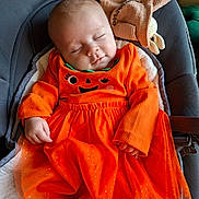 Jeanne a rejoint le concours — aidez-le/la à gagner de superbes lots ! baby, sleeping, orange_dress, pumpkin_outfit, infant, cushion, blanket, knitted_toy, baby_seat, cozy, cute, peaceful, child, portrait, indoors, soft_lighting, clothing, hand, face, toddler