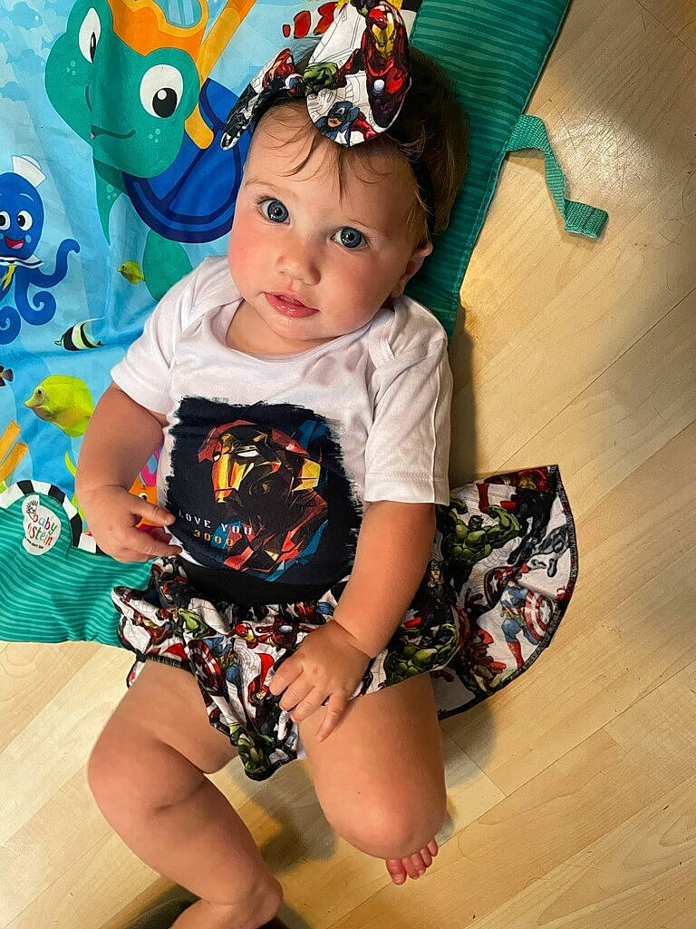 Elizabeth is registered to the contest to win money with this photo: baby, baby_toddler_clothing, cheek, child, electric_blue, face, fashion_accessory, fun, happy, head, headpiece, headwear, human_leg, knee, pattern, person, shorts, sitting, sleeve, t_shirt