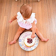 Gianna is registered to the contest to win money with this photo: baby, birthday, cake, celebration, child, eating, floor, frosting, happy, infant, indoor, messy, overhead_view, party, pink_clothing, portrait, sitting, sweet_food, wooden_floor, first_birthday