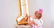 Gianna joined the competition — help win amazing prizes! baby, child, toddler, birthday, number_one, balloon, crown, pink, dress, standing, reaching, back_view, indoors, studio, wooden_floor, stool, celebration, portrait, party, family_event