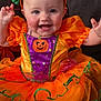 Nova is registered to the contest to win money with this photo: baby, child, smile, halloween, costume, pumpkin, orange, purple, green_bow, headband, tutu, sitting, couch, cushion, happy, cute, indoors, face, person, celebration