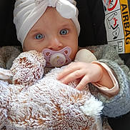 Elina a rejoint le concours — aidez-le/la à gagner de superbes lots ! baby, pacifier, stuffed_animal, hat, car_seat, airbag_warning, blue_eyes, hand, clothing, blanket, child, portrait, cute, infant, cozy, soft_toy, indoor, sitting, warm, young_child