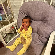 Trustin is registered to the contest to win money with this photo: baby, child, yellow_onesie, bee_pattern, cushioned_chair, indoor, infant, four_months, window_blind, sitting, fingers_in_mouth, curious, cute, wooden_chair, baby_clothing, home_interior, shelf, baby_accessories, smiling, portrait