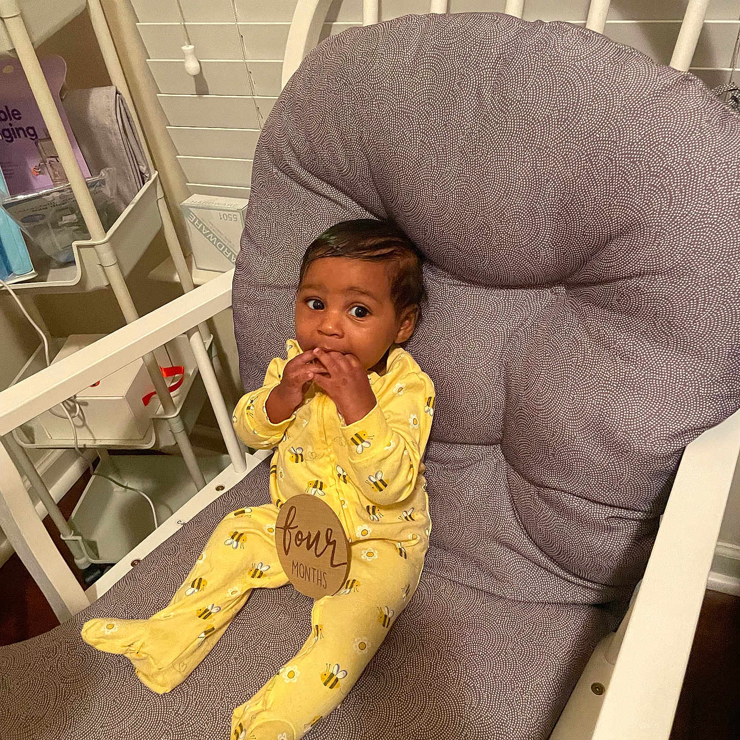 Trustin is registered to the contest to win money with this photo: baby, baby_accessories, baby_clothing, bee_pattern, child, curious, cushioned_chair, cute, fingers_in_mouth, four_months, home_interior, indoor, infant, portrait, shelf, sitting, smiling, window_blind, wooden_chair, yellow_onesie