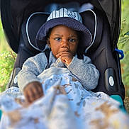 Nael a rejoint le concours — aidez-le/la à gagner de superbes lots ! toddler, child, baby, hat, bucket_hat, stroller, blanket, thumb_sucking, cozy_clothing, outdoor, portrait, face, cute, young_child, seat, baby_blanket, nature, greenery, close_up, casual