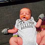 Jack is registered to the contest to win money with this photo: baby, infant, sleeping, pacifier, couch, sofa, blanket, mittens, clothing, onesie, portrait, indoor, sitting, lying_down, relaxed, cozy, face, child, patterned_fabric, home