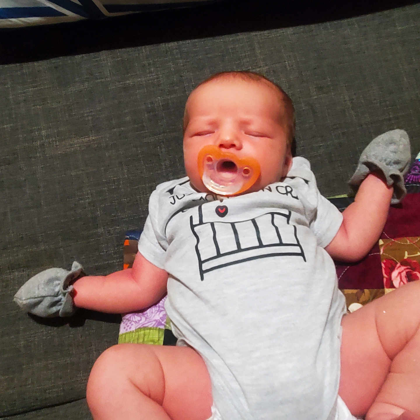 Jack is registered to the contest to win money with this photo: baby, infant, sleeping, pacifier, couch, sofa, blanket, mittens, clothing, onesie, portrait, indoor, sitting, lying_down, relaxed, cozy, face, child, patterned_fabric, home