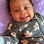 Kaylani is registered to the contest to win money with this photo: baby, smiling, face, infant, onesie, floral_pattern, lying_down, purple_blanket, happy, cute, child, skin, clothing, portrait, young, cheerful, indoors, head, closeup, baby_girl