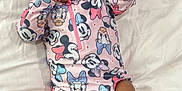 Kaylani is registered to the contest to win money with this photo: baby, infant, smiling, onesie, disney, mickey_mouse, donald_duck, daisy_duck, pluto, bed, white_sheet, clothing, cute, child, person, portrait, lying_down, hand_near_mouth, soft_lighting, indoor