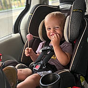 Graynger is registered to the contest to win money with this photo: toddler, child, car_seat, lollipop, smile, happy, seatbelt, vehicle_interior, window, daylight, casual_clothing, safety_harness, black_car_seat, cute, portrait, young_child, seat_cup_holder, car, sitting, fun