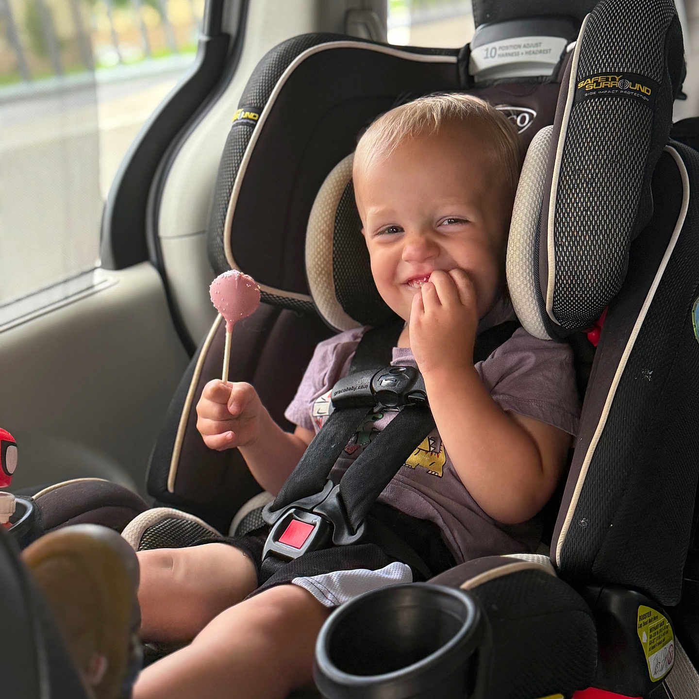 Graynger is registered to the contest to win money with this photo: black_car_seat, car, car_seat, casual_clothing, child, cute, daylight, fun, happy, lollipop, portrait, safety_harness, seat_cup_holder, seatbelt, sitting, smile, toddler, vehicle_interior, window, young_child