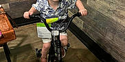 Whitley joined the competition — help win amazing prizes! bike, chair, child, curly_hair, flooring, footwear, green_plants, handlebars, happy, indoor, person, playful, shirt, shorts, smile, table, toy, training_wheels, wood_paneling, young