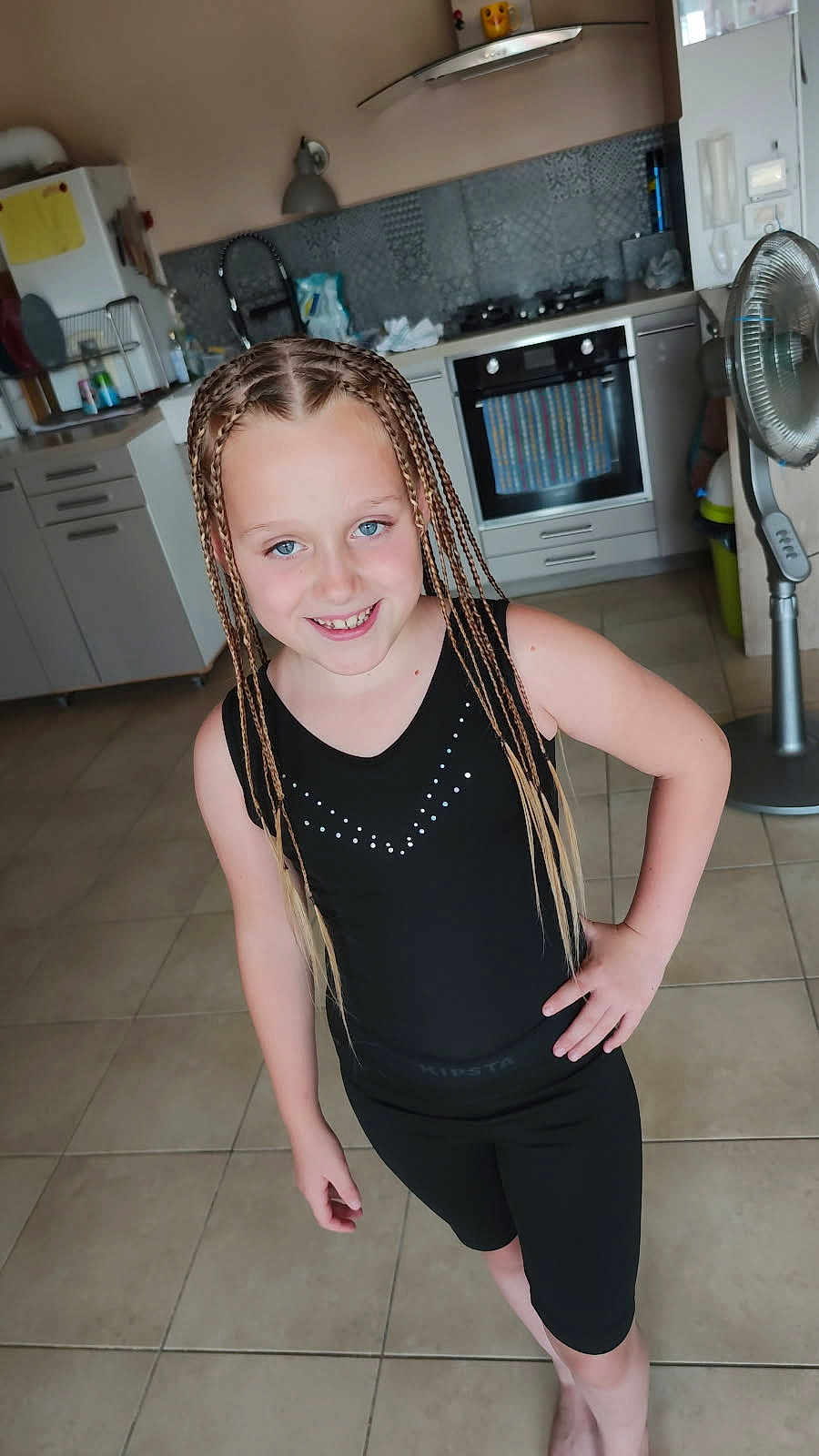 Mathéa participe au concours pour gagner de l'argent avec cette photo : child, girl, braids, smile, black_clothing, kitchen, floor_tiles, standing, pose, modern_kitchen, appliances, oven, fan, cabinet, countertop, indoor, person, happy, casual, youth