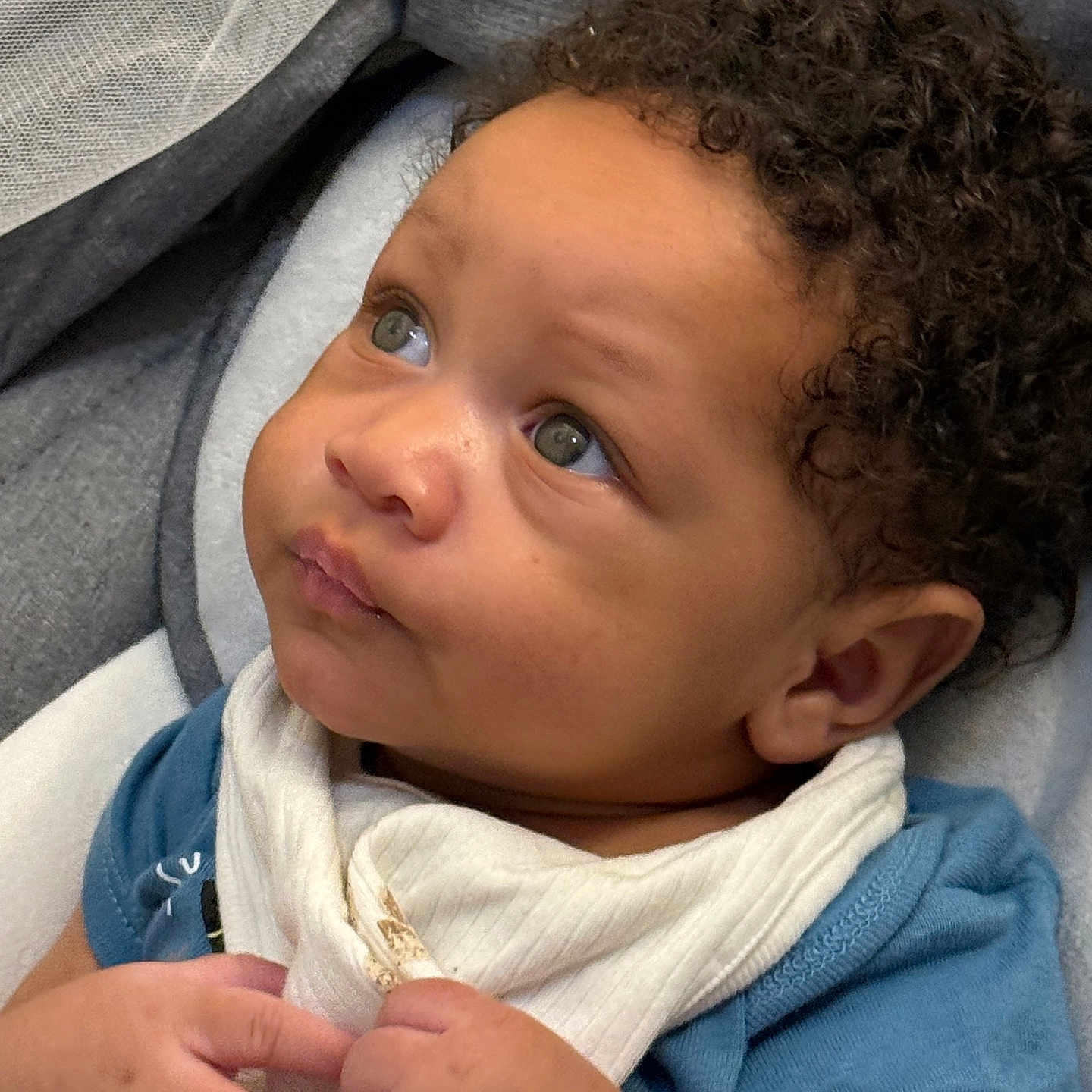 Micha joined the competition — help win amazing prizes! baby, infant, curly_hair, green_eyes, blue_shirt, bib, blanket, closeup, cute, child, indoors, portrait, hands, skin, expression, person, newborn, face, toddler, young_child