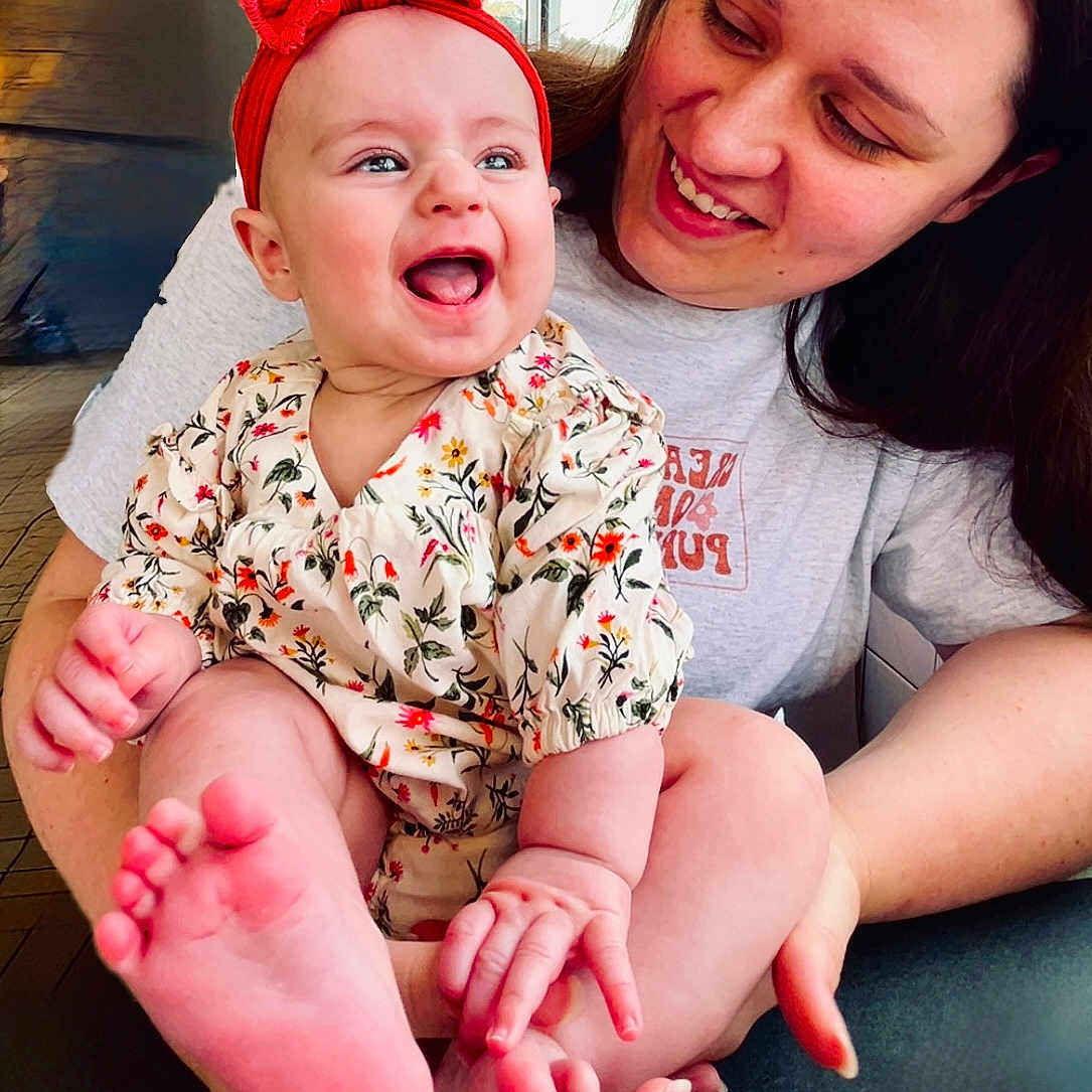 Ruby is registered to the contest to win money with this photo: affection, baby, casual_clothing, child, family, floral_outfit, foot, hair, hands, happy, headband, holding, indoor, laughing, person, portrait, skin, smile, table, woman
