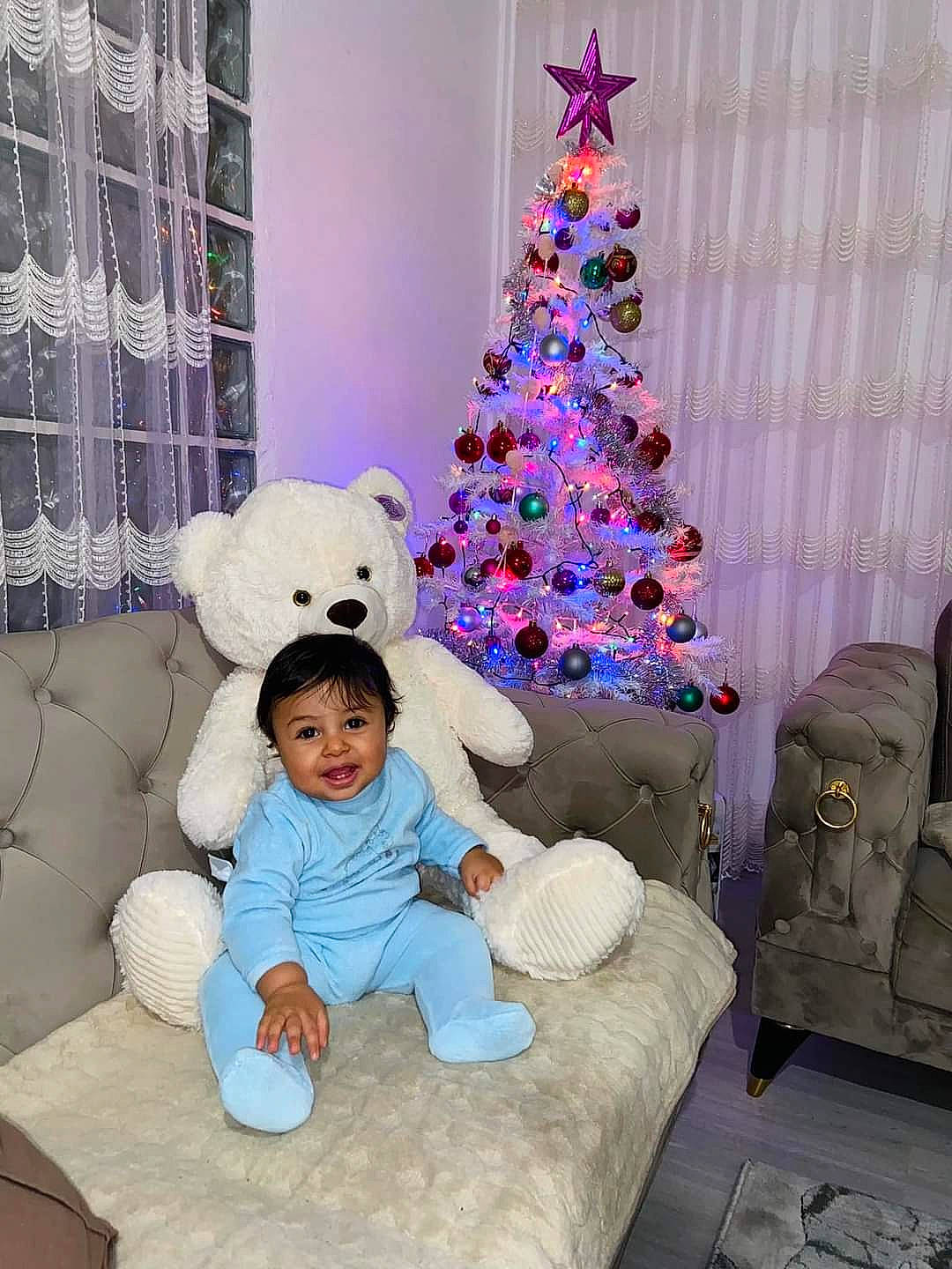 Menan participe au concours pour gagner de l'argent avec cette photo : christmas, christmas_decoration, christmas_ornament, christmas_tree, comfort, couch, event, holiday, holiday_ornament, interior_design, living_room, ornament, person, purple, teddy_bear, textile, toddler, toy, tree, white