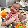 baby, smiling, pink_clothing, activity_center, toy, indoor, living_room, baby_swing, carpet, furniture, child, cute, happy, face, infant, play, seat, home, person, portrait