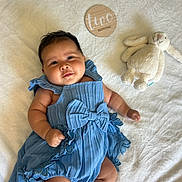 Ayana is registered to the contest to win money with this photo: baby, infant, child, portrait, smiling, blue_outfit, dress, bow, blanket, plush_toy, bunny, nursery, lying_down, indoor, close_up, happy, face, wooden_sign, two_months, family_photo