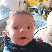 Harley joined the competition — help win amazing prizes! baby, infant, child, face, eyes, mouth, hair, bib, hand, arm, holding, close_up, portrait, indoor, kitchen, countertop, toaster, appliance, fairy_lights, soft_focus