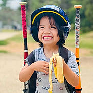 Zyrus is registered to the contest to win money with this photo: child, smiling, helmet, banana, baseball_bats, outdoor, sports, happy, person, short_sleeve_shirt, backpack, grinning, toy, play, summer, recreation, fun, youth, active, portrait