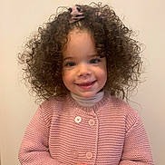 Késia participe au concours pour gagner de l'argent avec cette photo : child, toddler, curly_hair, pink_sweater, smiling, portrait, indoor, hands_clasped, cute, young, person, face, happy, buttoned_sweater, long_sleeves, light_background, fashion, cute_expression, warm_clothing, innocent