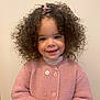 child, toddler, curly_hair, pink_sweater, smiling, portrait, indoor, hands_clasped, cute, young, person, face, happy, buttoned_sweater, long_sleeves, light_background, fashion, cute_expression, warm_clothing, innocent