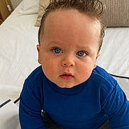 Hélio participe au concours pour gagner de l'argent avec cette photo : toddler, child, baby, blue_sweater, grey_pants, bed, pillows, indoor, curly_hair, blue_eyes, person, cute, sitting, looking_up, toy, hand, cozy, soft_lighting, portrait, casual