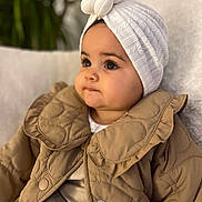 Agathe participe au concours pour gagner de l'argent avec cette photo : baby, infant, headwrap, white_hat, quilted_jacket, brown_coat, chubby_cheeks, big_eyes, portrait, close_up, indoor, couch, blanket, plant, sitting, fashion, cute, eyelashes, soft_lighting, warm_colors