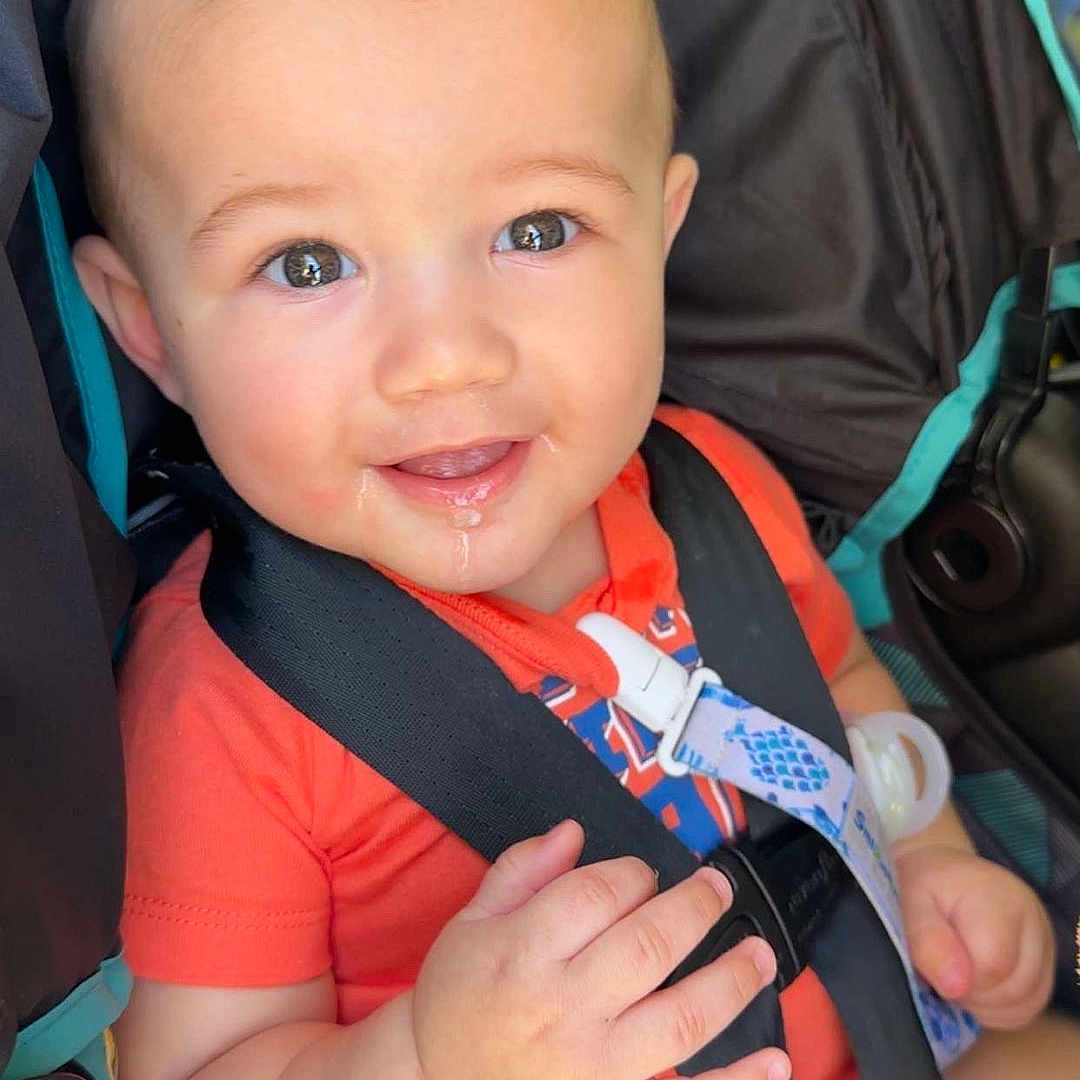 Miguel is registered to the contest to win money with this photo: baby, car_seat, child, cute, drool, eyes, face, hand, happy, head, indoor, infant, orange_clothing, person, portrait, safety, seatbelt, skin, smiling, straps