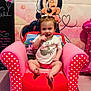 baby, child, smiling, pink_chair, polka_dots, birthday, minnie_mouse, cartoon, toddler, indoor, party, celebration, cute, happy, girl, clothing, decorations, toy, sitting, portrait