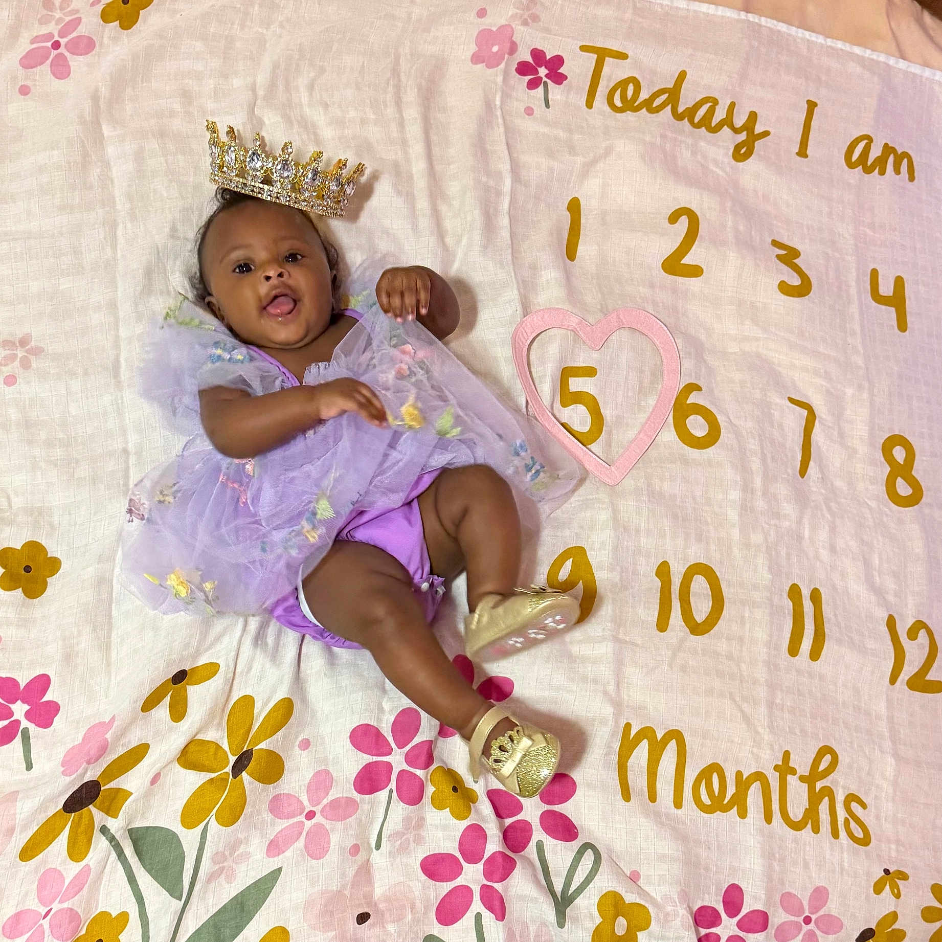 Hilani joined the competition — help win amazing prizes! baby, celebration, child, clothing, colorful, crown, cute, floral_blanket, golden_shoes, happy, headwear, heart, indoors, infant, lying_down, months, numbers, portrait, purple_dress, smiling