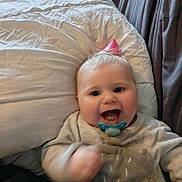 Liluo participe au concours pour gagner de l'argent avec cette photo : baby, pacifier, party_hat, smiling, motion_blur, bed, pillow, blanket, clothing, infant, happy, face, child, cute, indoors, person, celebration, soft_toys, cozy, lifestyle