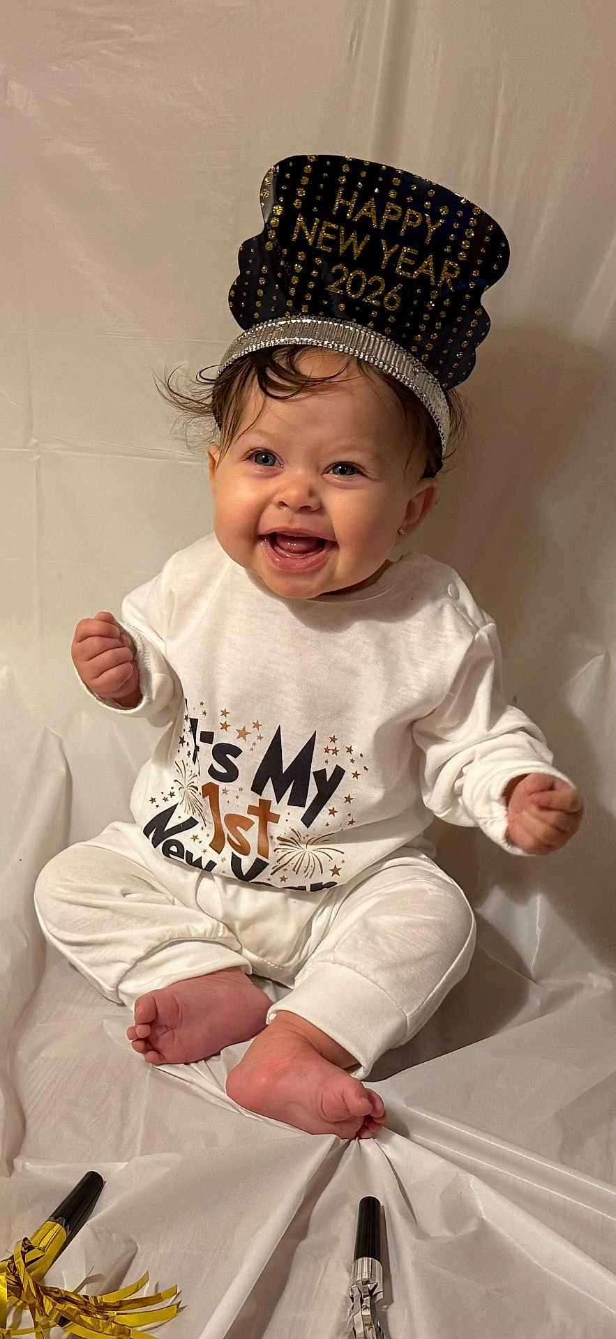 Aubrey is registered to the contest to win money with this photo: baby, child, smiling, happy, celebration, new_year, party_hat, white_clothing, sitting, tooth, face, foot, hand, background, festive, indoors, party_blowers, headwear, cute, portrait