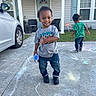 child, toddler, smiling, chalk, driveway, sidewalk, house, door, window, car, grass, shirt, jeans, sneakers, outdoor, play, fun, person, daylight, curly_hair