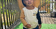 Ace is registered to the contest to win money with this photo: toddler, child, hat, straw_hat, outdoor, deck, wooden_rail, green_carpet, jeans, long_sleeve_shirt, two_tone_clothing, sunny_day, leafy_background, person, footwear, black_shoes, nature, sky, clouds, casual_wear